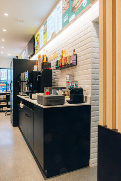 Coffee shop checkout counter with black cabinetry, white subway tile backsplash, menu boards above, and product displays on shelving