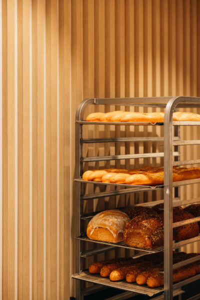 Metal bakery display rack with fresh bread loaves and rolls on multiple shelves against wooden wall