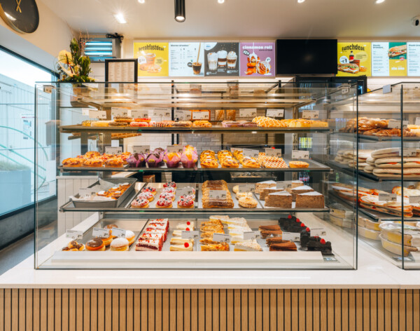 Bakery display case with tiered glass shelving showcasing pastries, breads and decorated cakes in a specialty food retail environment