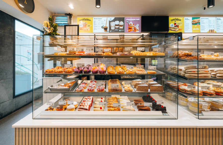 Bakery display case with tiered glass shelving showcasing pastries, breads and decorated cakes in a specialty food retail environment
