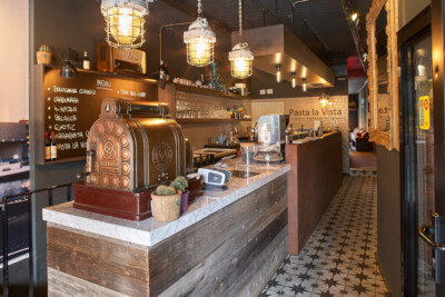 Horeca checkout counter with marble top, vintage brass espresso machine, pendant lighting, and brick backsplash in specialty food retail setting