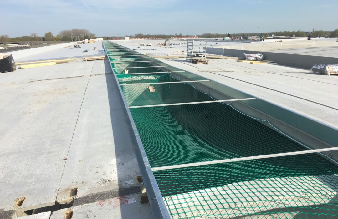 Industrial roofing construction with green mesh safety netting on concrete roof deck