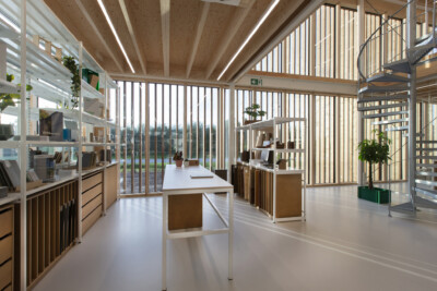 Modern office showroom with Pitch shelving, white desks, spiral staircase, and floor-to-ceiling windows overlooking landscape