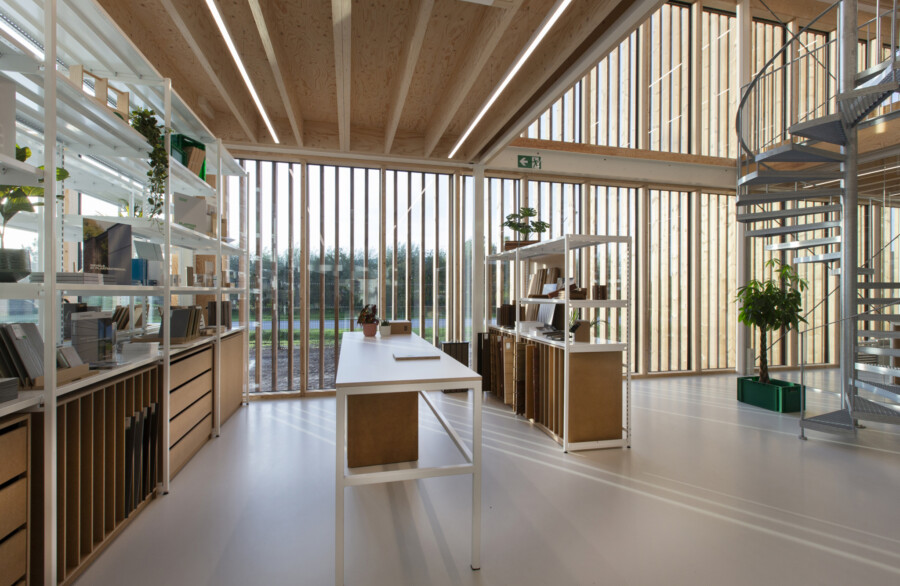 Modern office showroom with Pitch shelving, white desks, spiral staircase, and floor-to-ceiling windows overlooking landscape