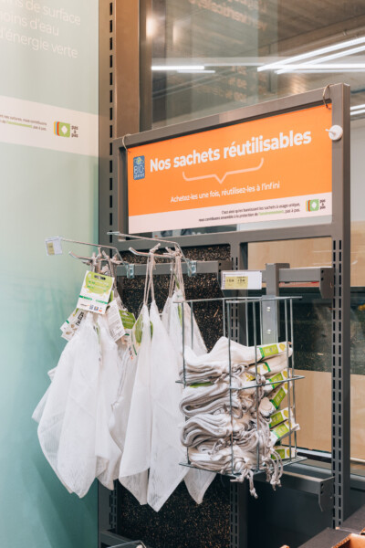 Reusable mesh shopping bags displayed on retail fixture with orange promotional signage in supermarket