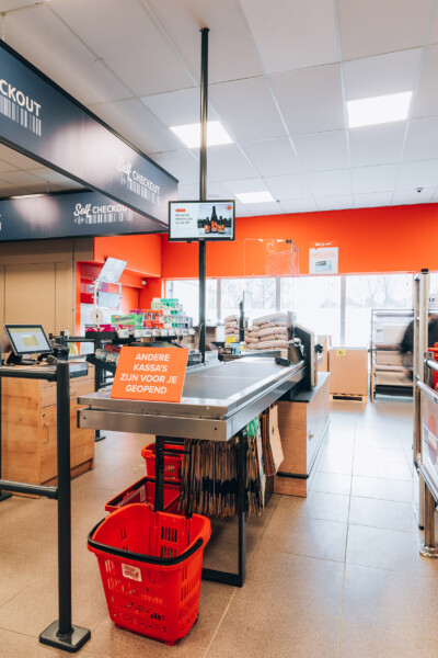 Carrefour Market checkout area with red shopping baskets, self-checkout signage, orange wall branding, and Pitch shelving display