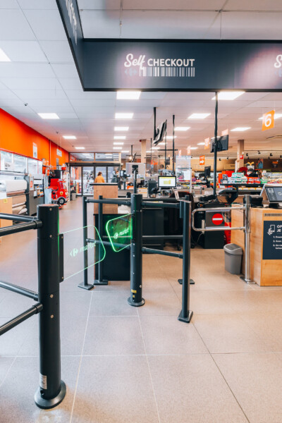 Self-checkout area with queue management barriers and neon market signage in supermarket