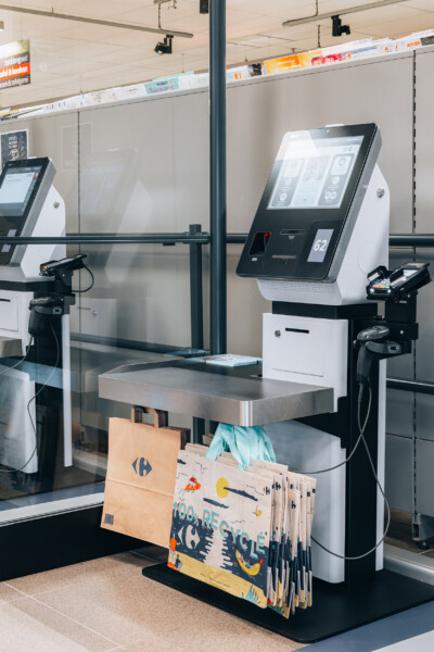 Self-service checkout kiosks with touchscreen displays and bagging area in supermarket setting