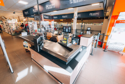 Carrefour Market checkout area with self-checkout counters, stainless steel transaction surfaces, and shelving in background