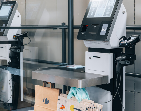 Self-service checkout kiosks with touchscreen displays and bagging area in supermarket setting