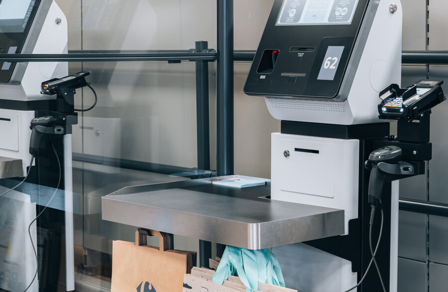 Self-service checkout kiosks with touchscreen displays and bagging area in supermarket setting