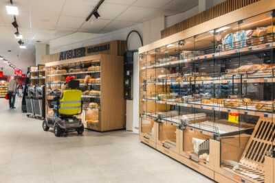 Carrefour Market bakery section with Pitch 41 shelving displaying bread and pastries, staff member restocking on mobility device