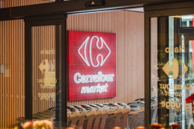 Carrefour Market storefront with red neon logo sign and wooden vertical slat design