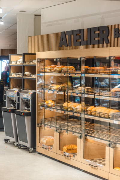 Carrefour Market bakery display with multi-tier black wire shelving showcasing fresh bread and pastries, wooden facade with vertical slat design