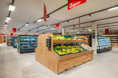 Carrefour Market supermarket produce display with wooden fruit stand featuring bananas, refrigerated cases, and red price signage