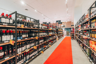 Delhaize wine section with Pitch 25 shelving displaying red and white wines with promotional signage and orange aisle runner
