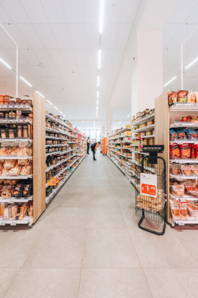 Delhaize supermarket aisle with Pitch shelving displaying packaged goods under bright linear ceiling lights