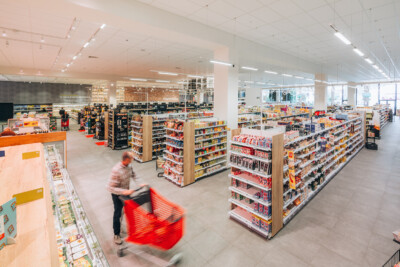 Delhaize supermarket interior with Pitch shelving displaying packaged goods, checkout counter, and modern retail layout
