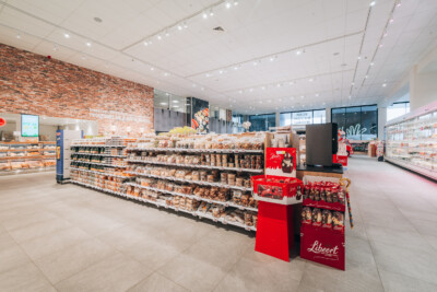 Delhaize supermarket interior with Pitch 25 shelving displaying packaged food products and red promotional displays