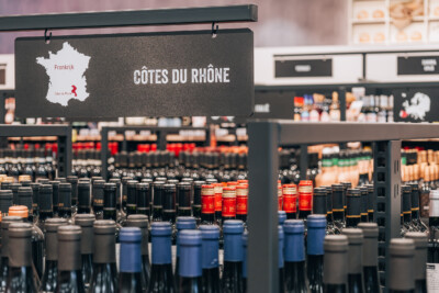 Côtes du Rhône wine section with Pitch 25 shelving displaying bottles with blue and red capsules in Delhaize supermarket