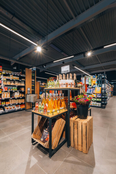 Delhaize supermarket interior with orange-themed retail displays, Pitch shelving systems, and beverage merchandising