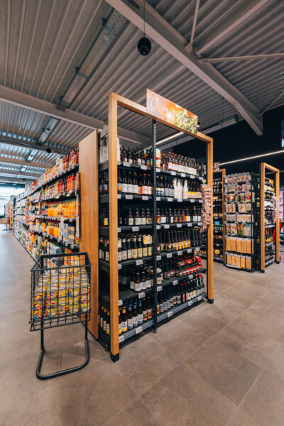 Wooden-framed shelving display with black shelves stocked with packaged food products and beverages in supermarket aisle