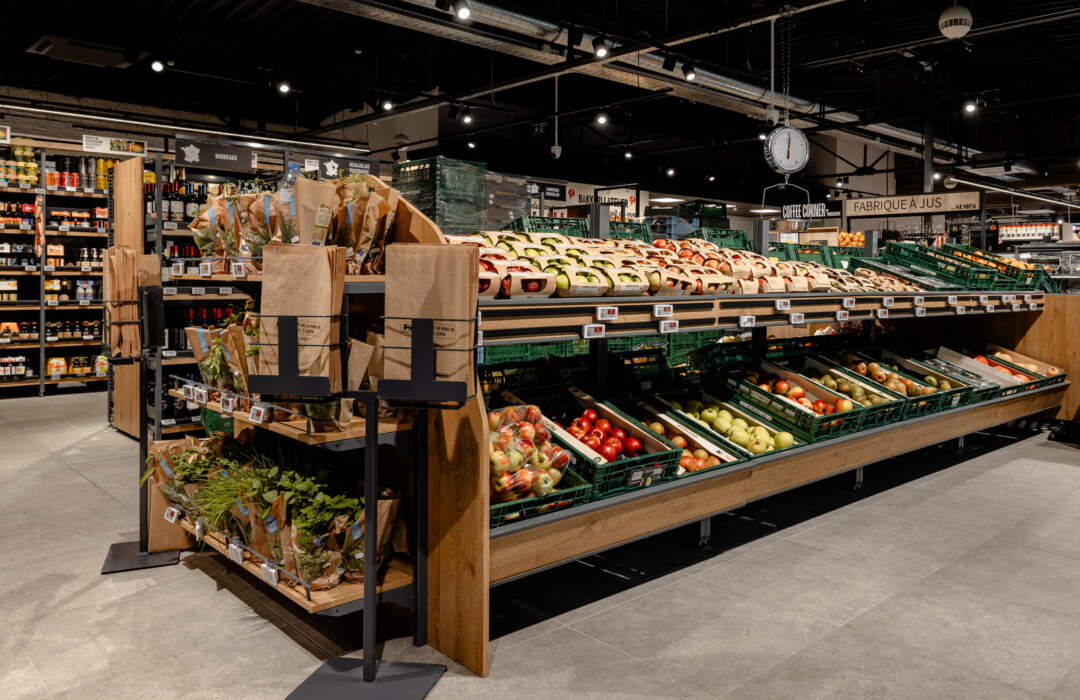 Produce display with fresh vegetables and baked goods in modern supermarket produce section with wooden shelving and signage