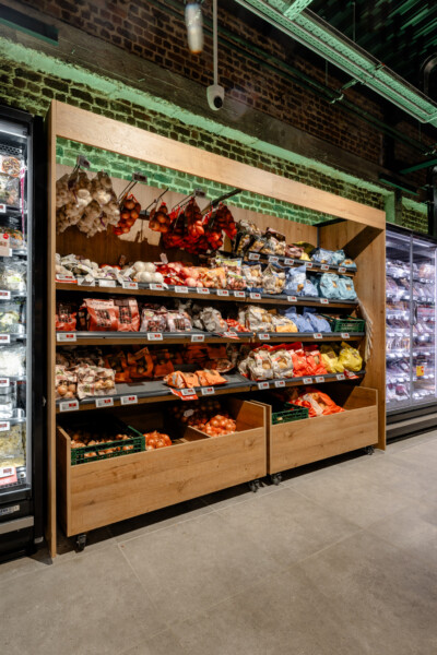 Pitch 25 wooden shelving display with fresh produce, vegetables and hanging goods in Delhaize supermarket