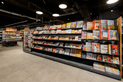 Pitch 25 shelving with books and magazines in Delhaize supermarket, featuring black metal shelves with angled display sections