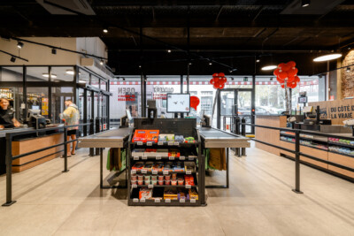 Proxy Delhaize supermarket interior with central promotional display, checkout counters, and Pitch shelving in grocery sector
