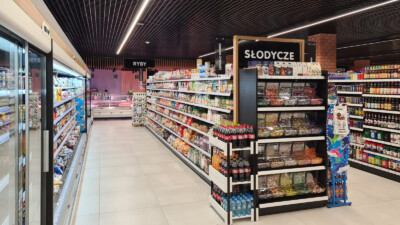 Specialty food store with Pitch 25 shelving displaying packaged goods, deli counter with refrigerated display, and organized product sections