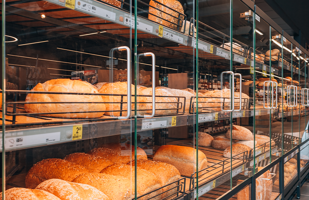 Bakery display with multiple shelves of fresh bread and rolls behind glass doors with metal handles