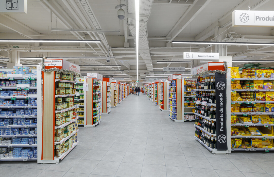 Supermarket aisle with Pitch 25 shelving displaying packaged goods, frozen products, and branded merchandise under industrial ceiling