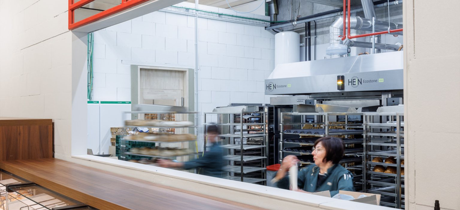 Delhaize Oudenaarde bakery counter with HEN ecostone display case, open kitchen shelving, and red shopfitting frame