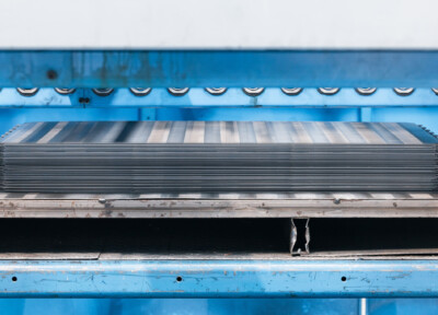 Stack of metal shelf panels with horizontal ribbing, blue industrial frame and support structure