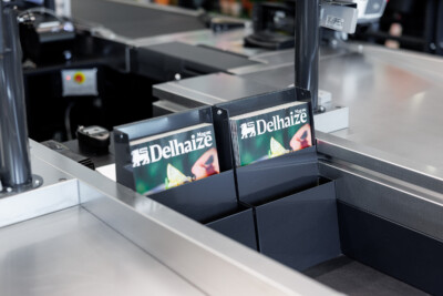 Delhaize checkout counter displays with black shelving and branded signage in supermarket setting