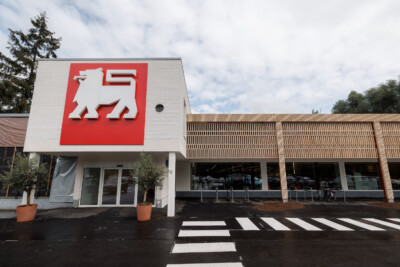 Delhaize logo on modern retail storefront with parking garage