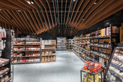 Delhaize supermarket aisle with Pitch shelving displaying packaged goods and beverages under wooden ceiling design