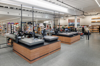 Delhaize supermarket checkout area with multiple Gondella checkout counters, shelving displays, and modern retail layout