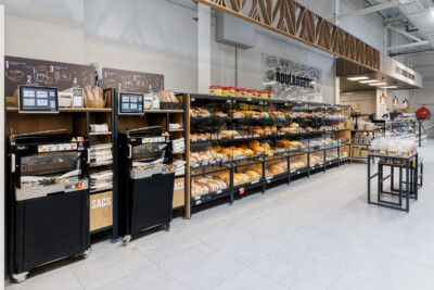 Delhaize bakery section with Pitch 25 shelving displaying bread and pastries, self-checkout kiosks, and boulangerie signage