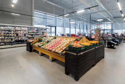 Delhaize supermarket produce display with Gondella yellow and black wooden gondolas showcasing packaged goods and fresh fruit