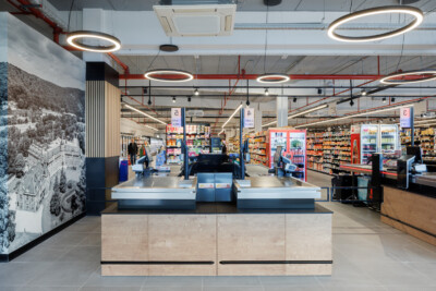 Delhaize supermarket checkout area with Gondella counter solutions, shelving displays, and circular ceiling lights