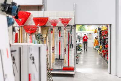Garden tool display with red leaf rakes and brooms on pegboard shelving in retail store