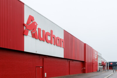 Auchan supermarket exterior with red brick base and corrugated metal upper facade displaying Auchan logo and signage