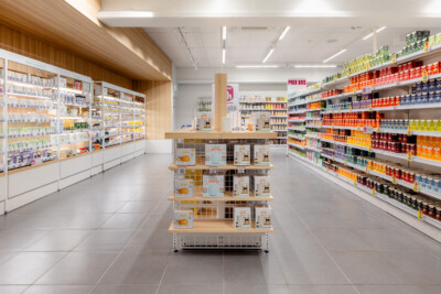 Delhaize supermarket aisle with Pitch shelving displaying health & beauty and grocery products, central display stand with wooden shelves