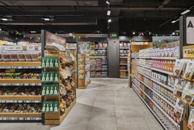 Spar supermarket aisle with Pitch shelving displaying packaged goods, beverages, and branded products under yellow and colored bunting