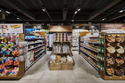 Supermarket aisle with Pitch shelving displaying packaged goods, bakery products in baskets, and beverages; specialty food retail layout
